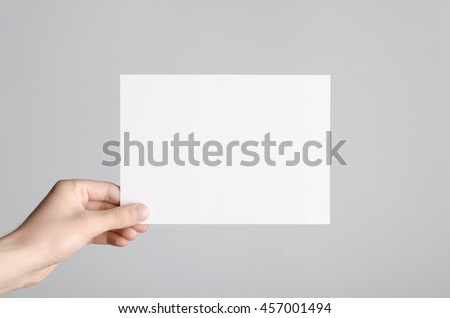 A5 Flyer / Invitation Mock-Up - Male hands holding a blank flyer on a gray background. Royalty-Free Stock Photo #457001494