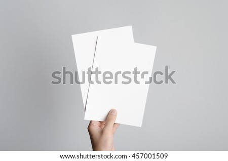 A5 Flyer / Invitation Mock-Up - Male hands holding blank flyers on a gray background. Royalty-Free Stock Photo #457001509