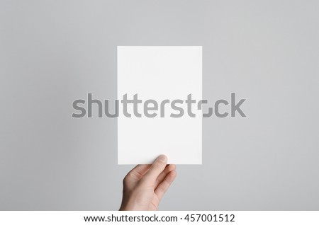 A5 Flyer / Invitation Mock-Up - Male hands holding a blank flyer on a gray background. Royalty-Free Stock Photo #457001512