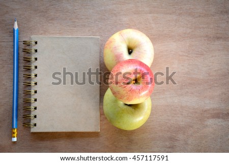 Notebook, pencil, apple on a wooden floor.