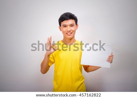 A boy in yellow shirt makes OK symbol with his hand and blank page.