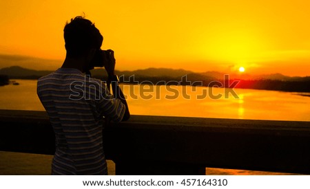 A silhouette of man taking photos of sunset with digital camera with the background of orange sunset. stock photo . copy space