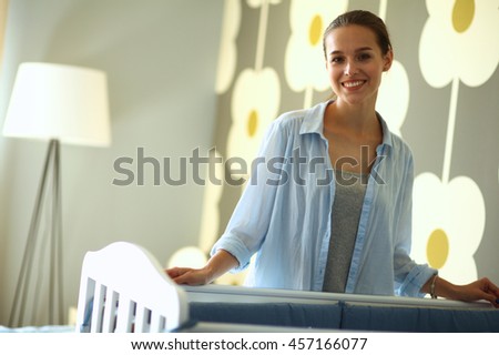 Young woman standing near children's cot.