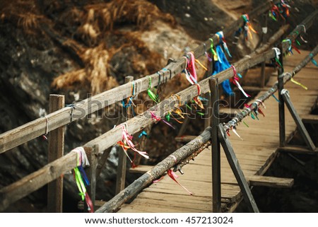 Wooden bridge above mountain river in autumn with traditional buddhism ribbons. Nature background.