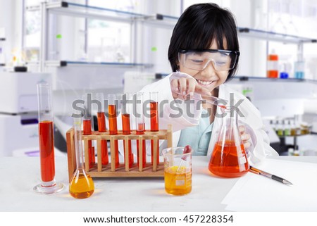 Photo of a little girl doing chemistry research while wearing glasses and coat in the library