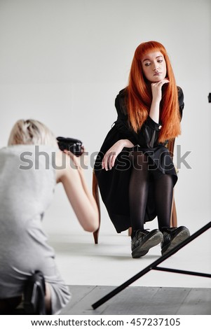 Fashion model girl sitting on chair posing to photographer on white in Studio
