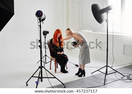 The photographer straightens hair fashion model sitting on chair on white background in Studio