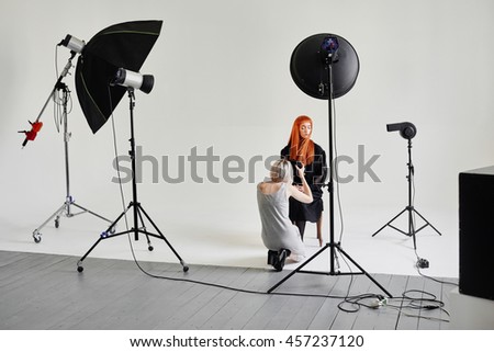 Girl photographer photographing fashion model in black sitting on a chair on white background in Studio