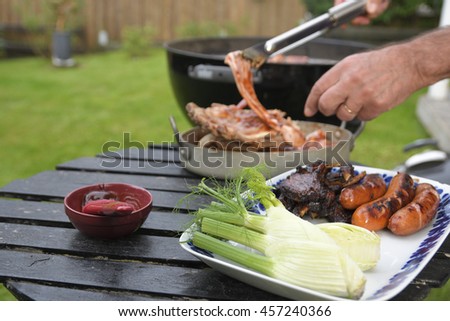 Plate with fennel and grilled sausages and ribs and in the background hand with pincers grabbing a spare-rib, picture from Sweden.