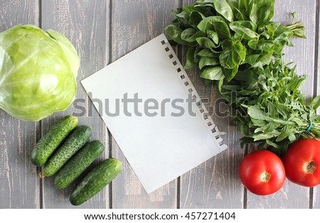Paper leaf and composition of vegetables on grey wooden desk. Tomato, cucumber, cabbage, basil, arugula. Top view. Modern photography. The best for recipies.