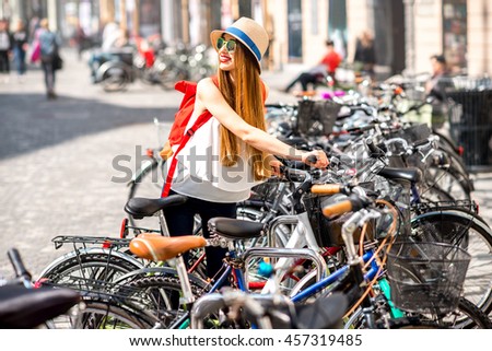 Young female tourist taking the bicycle from the parking in the old Eropean city center. Bicycle renting.