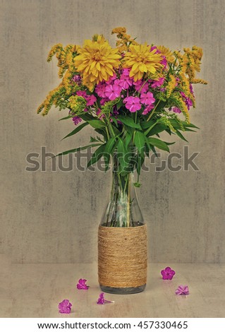 a bouquet of flowers of goldenrod, phlox and lilies in a glass bottle. toned photo
