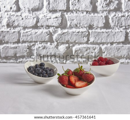 strawberry raspberry blueberry behind brick wall white backround