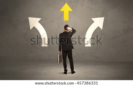 A confused businessman facing a grey urban wall with a yellow arrow pointing in the right direction concept