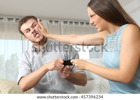 Couple or friends fighting for a mobile phone sitting on a couch at home Royalty-Free Stock Photo #457396234