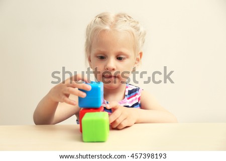 Funny little girl hiding behind white table and taking colourful cubes