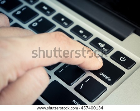 Finger pushing delete key on laptop keyboard