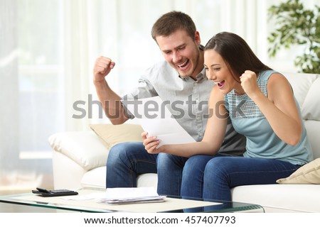 Excited couple reading a letter together sitting on a sofa in the living room at home Royalty-Free Stock Photo #457407793