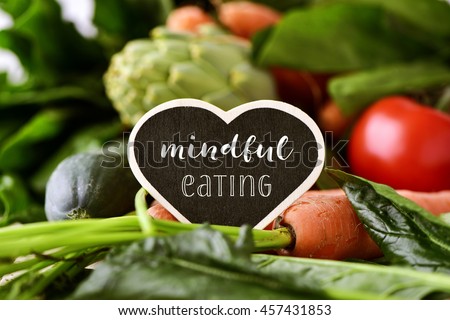 closeup of a heart-shaped chalkboard with the text mindful eating placed on a pile of some different raw vegetables, such as cucumbers, tomatoes, carrots, artichokes, green peppers and zucchinis Royalty-Free Stock Photo #457431853