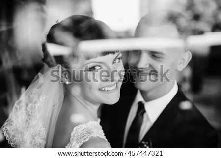 Black and white picture of a smiling bride standing with a groom behind a window