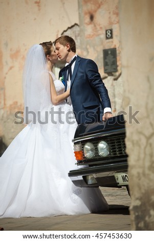 Kissing wedding couple leans to an old car