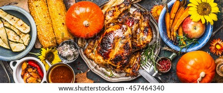 Thanksgiving Day food. Various grilled vegetables ,roasted chicken or turkey and pumpkin with sunflowers decoration on dark background, top view, banner