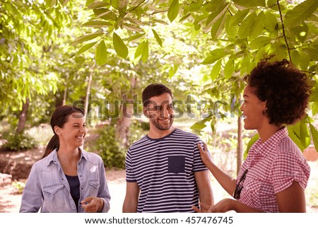 Three healthy friends chatting and laughing together in the dappled afternoon sunshine with some trees around them wearing casual clothing