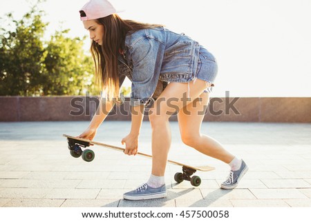 Young girl putting longboard on the pavement in park 
