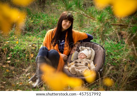Portrait of beautiful young brunette girl with her baby in the autumn forest. The colorful leaves. The concept of motherhood