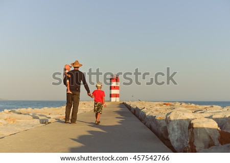 Back view of male with kids walking to the red lighthouse, sunny outdoors background. Book cover concept design