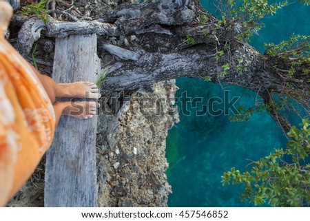 Highly Detailed Photo Woman Legs. Girl Looking Down Cliff Old Tree. Blue Ocean Water Blurred Background.Horizontal picture. Top View