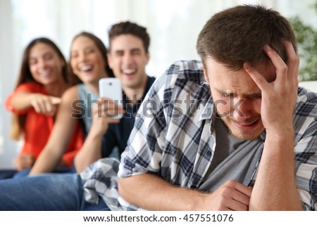 Friends bullying to a sad boy and taking photos with a smartphone for the social network Royalty-Free Stock Photo #457551076