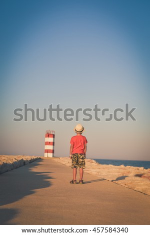 Back view of cute boy looking at ocean lighthouse on blue sky sunny outdoors background. book cover concept design