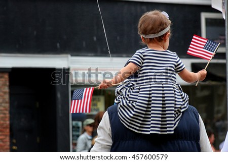 Young child on her fathers shoulder waving American Flags
