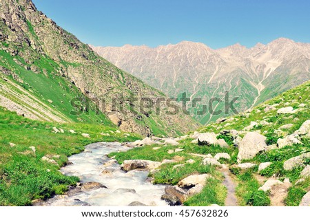 River on green meadow. High mountains and bright sky with clouds
