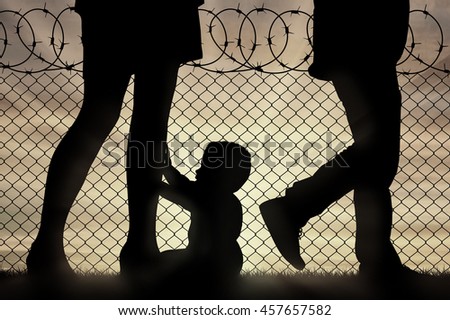 Refugee family concept. Silhouette of the child and parents legs refugees near the border fence