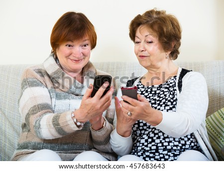 Smiling elderly friends sitting with smartphones in living room Royalty-Free Stock Photo #457683643