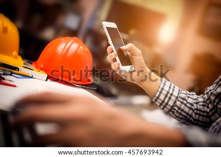 Photography of vintage picture style engineering working at construction office desk and holding mobile smartphone, architect engineer with new technology concept.