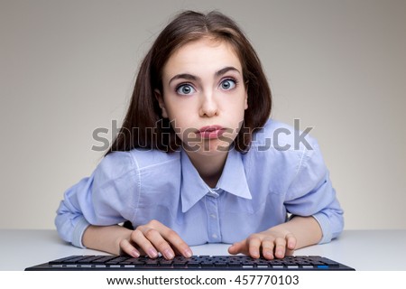 Silly young woman puffing cheeks and using computer keyboard on grey office desktop