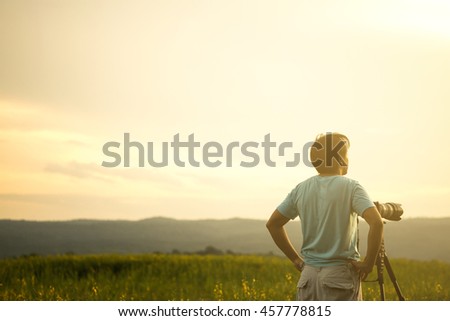 Nature photographer standing with camera and tripod taking photo in wild