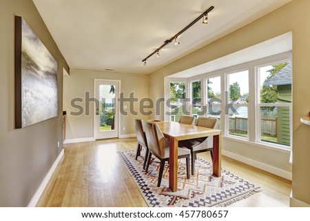 Cozy creamy tones dining room with wooden table set. There is old ethnic pattern rug on hardwood floor and contrast wall with mocha paint. Northwest, USA