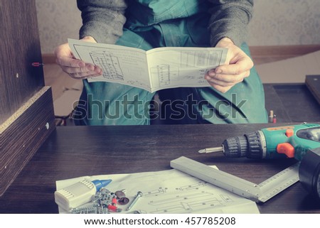 Frustrated man reading instruction and putting together self assembly furniture. DIY, new home and moving concept Royalty-Free Stock Photo #457785208