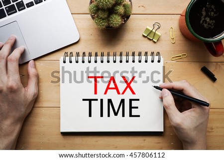 Person write word of "Tax Time" on notebook with laptop on wooden desk