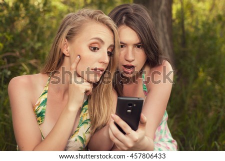 Two girls look at the phone's screen outdoors blonde and brunette is surprised