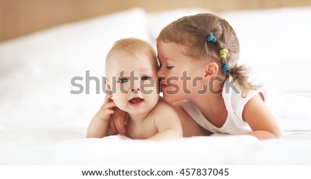 happy family sister kisses baby brother in bed