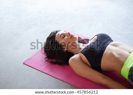 Young woman practicing in a yoga studio on pink mat and grey concrete floor. Shavasana or corps pose is the end of a class or practice with copyspace Royalty-Free Stock Photo #457856212