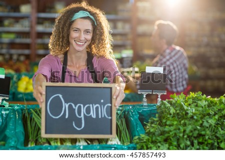 Portrait of smiling staff holding organic sign board in organic section of supermarket