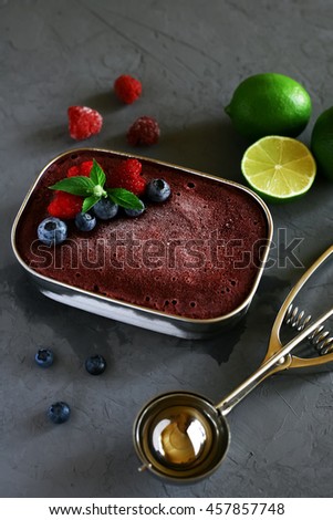Raspberry and blueberry homemade ice cream in a metal bowl, decorated with raspberries, blueberries, mint and Ice-cream scoop, raspberries, blueberries and lime on a gray background