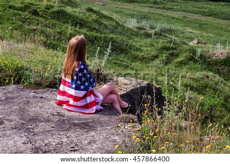 Girl sitting on large rocks holding flags of the United States
