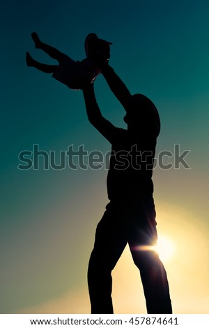 Joyful silhouette of father throwing up his child at sunset outdoors background